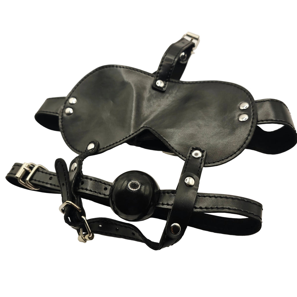 Black leather adult novelty harness with a ball gag and silver metal buckles and rivets, laid flat on a white fabric background.