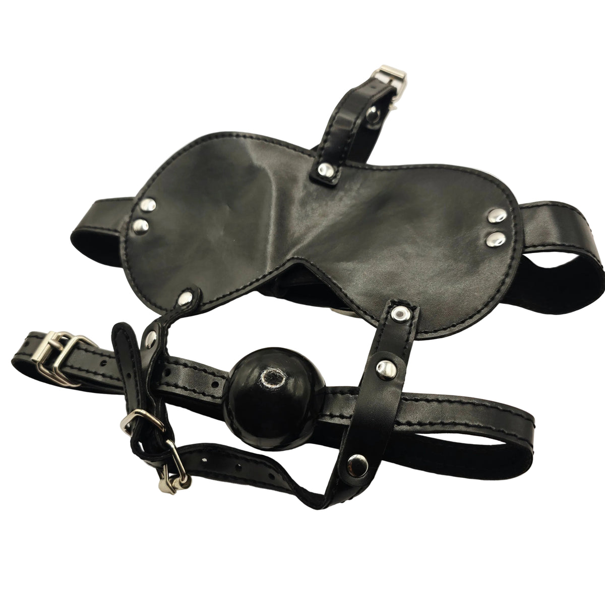 Black leather adult novelty harness with a ball gag and silver metal buckles and rivets, laid flat on a white fabric background.