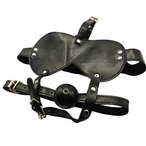 Black leather adult novelty harness with a ball gag and silver metal buckles and rivets, laid flat on a white fabric background.
