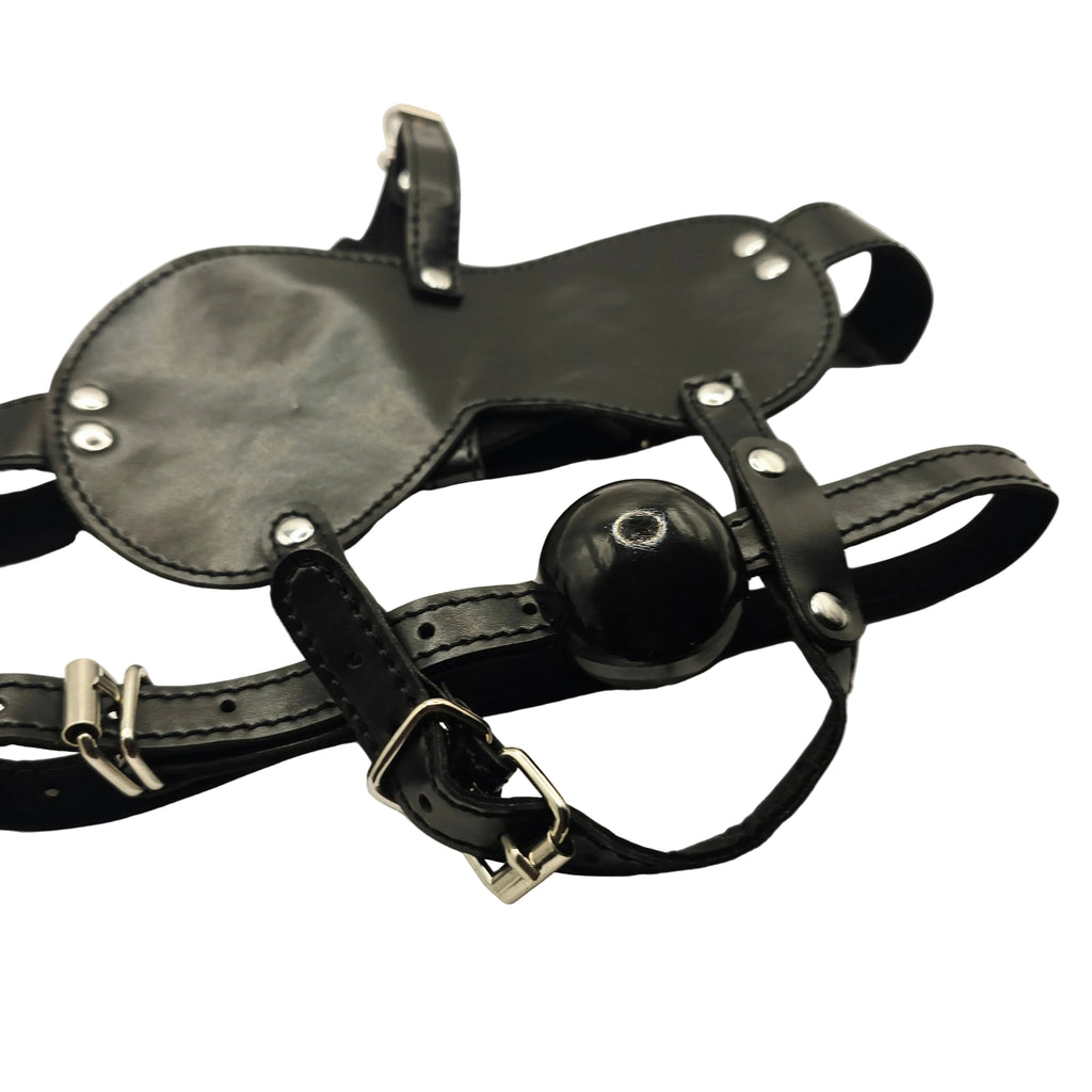 Black leather adult novelty gag harness with a glossy black ball gag and silver metal buckles, displayed on a white satin fabric background.