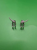 A pair of silver-toned metal earrings shaped like stylized animal legs with curved horns, displayed on a solid green background.