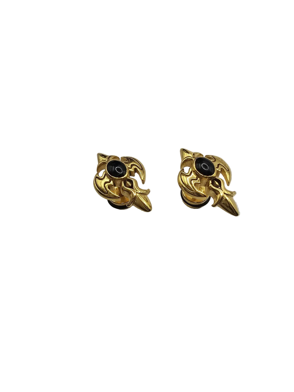 A pair of gold-toned gothic-style stud earrings with black circular centers, displayed on a textured light gray fabric background.