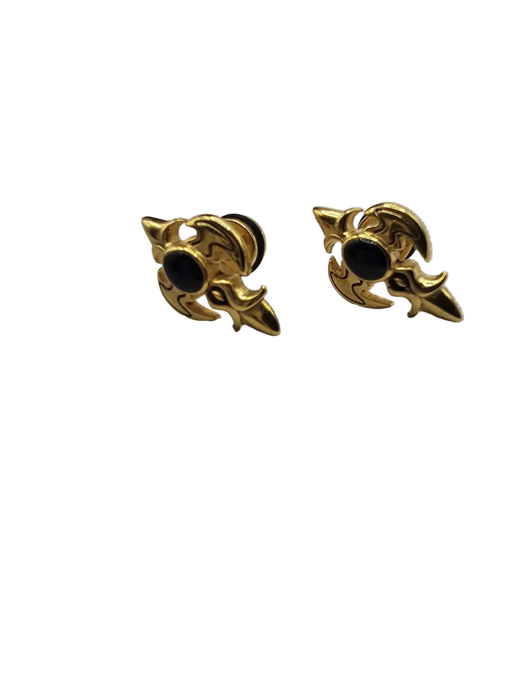 A pair of gold-toned gothic-style stud earrings with black circular centers, displayed on a textured light gray fabric surface.