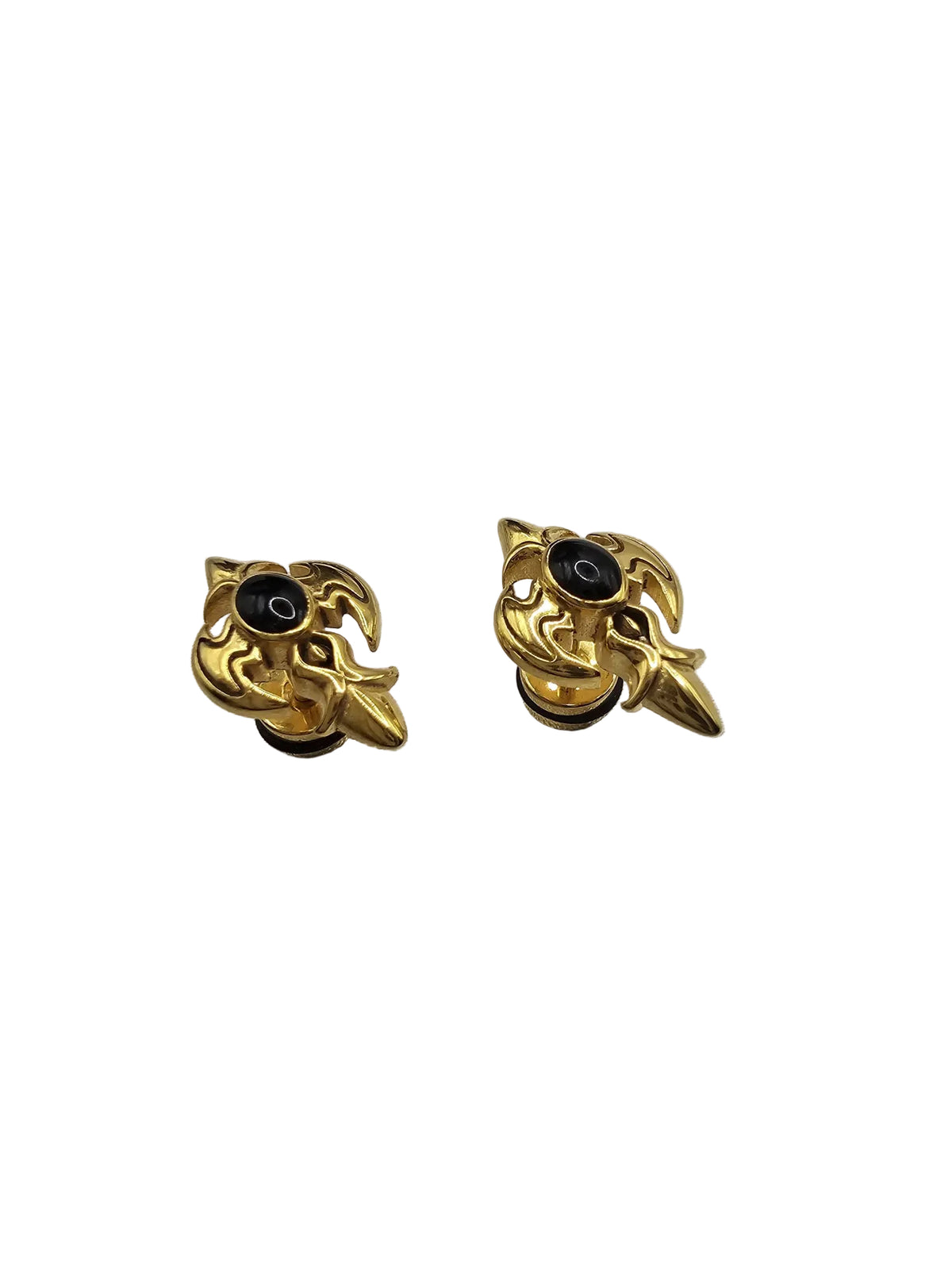 A pair of gold-toned gothic-style stud earrings with a central black circular detail, displayed on a textured light gray fabric background.